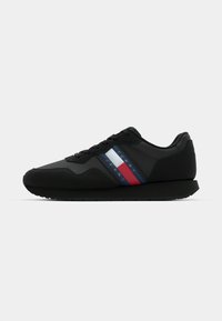 Schwarzer Sportschuh aus glattem Material, mit drei horizontalen Streifen in Blau, Weiß und Rot. Gummisohle mit strukturiertem Boden.