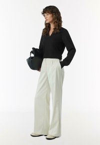 Schwarz langärmeliges Oberteil mit V-Ausschnitt, kombiniert mit ivoryfarbenen weiten Hosen. Die Accessoires umfassen eine schwarze Handtasche und helle Schuhe.