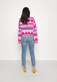 Stickad tröja med ett rosa och lila geometriskt mönster, med en kort design. Buren med ljusa tvättade jeans och gula klacksandaler.