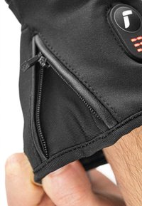 Gant noir avec un tissu texturé, une poche zippée et un bouton de contrôle avec des lumières indicatrices. Gros plan sur une main tenant le poignet.