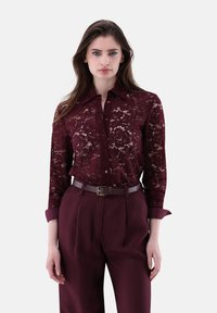 Burgunderfarbene Spitzenbluse mit Kragen und Knopfleiste, kombiniert mit hochgeschnittenen burgunderfarbenen Hose und einem passenden Gürtel mit Falten.