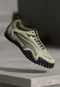Olivgrüner Sneaker mit strukturiertem Obermaterial, Nylon-Schnürsenkeln und einer genoppten schwarzen Gummisohle für besseren Halt. Puma-Logo an der Seite.