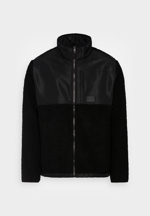 Black zip-up jacket with fleece lower sections and sleeves, smooth upper chest panel, stand collar, and a chest pocket on the left side.