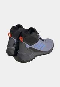Scarpe da trekking grigie e nere con accenti blu, tomaia strutturata, tallone rinforzato e suola con motivo; dotate di linguetta arancione.