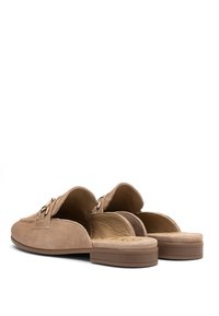 Scarpe slip-on in suede beige con apertura sul retro, caratterizzate da dettagli in metallo dorato e una soletta testurizzata, progettate per comfort e abbigliamento casual.