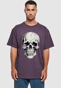 Lila bomulds T-shirt med et stort, detaljeret kraniumgrafik med revner, korte ærmer og et afslappet fit design.