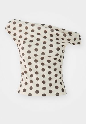 Bež pamukasta bluzica s širokim smešnim tačkama, koja ima uski kroj i prevrnute rukave.