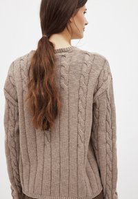 Bežinis megztinis su kabelių megzto dizaino, raukšlėtos tekstūros ir apvalaus iškirpimo, laisvo kirpimo ir nuleistomis pečių siūlėmis.