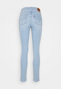 Vaqueros ajustados de color azul claro con una cintura alta, bolsillos traseros curvados y un parche de cuero marrón en la parte posterior. Textura de denim suave.