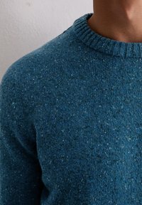 Niebieski sweter dziany z żeberkowym okrągłym dekoltem, z delikatnymi kropeczkami i równą teksturą, w ujęciu z góry, ukazującym górną część torsu.