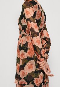 Blumenkleid mit schwarzem Hintergrund und großen, pfirsichfarbenen Rosenmustern. Hergestellt ausdurchsichtiger Stoff mit smockiertem Bund und Rüschensäumen.
