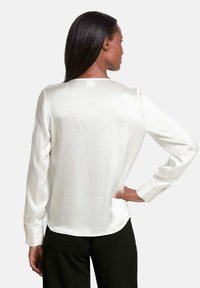 Witte satijnen blouse met lange mouwen en een subtiele glans, ronde zoom en knoopmanchetten, bekeken vanuit de achterkant. Gladde textuur en een ontspannen fit.