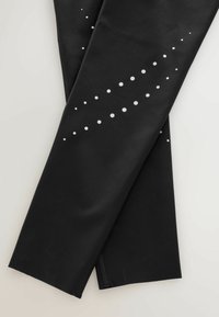 Leggings negre cu o textură netedă, având un model de puncte albe dispuse pe o linie diagonală pe o picior.