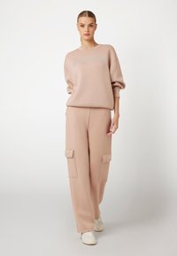 Šviesiai rožinė džemperis su apvalia iškirpte ir laisvu siluetu, derinamas su atitinkamais cargo kelnėmis, turinčiomis kišenes ir baltomis sportinėmis batelėmis.