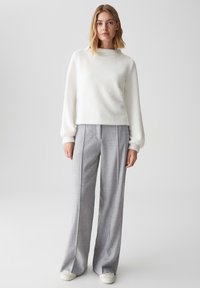Maglione bianco e soffice con collo alto, abbinato a pantaloni ampi a fantasia grigio chiaro e scarpe bianche semplici.