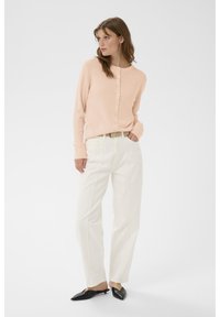 Hellrosa gerippte Strickjacke mit Knopfverschluss, kombiniert mit weißen, gerade geschnittenen Hosen mit Seitennaht; schwarze spitze Mules vervollständigen den Look.