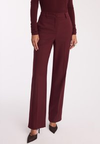 Burgundowe dopasowane spodnie z szerokimi nogawkami, z zapięciem na guzik i szlufkami na pasek. Wykonane z gładkiego materiału, z wyraźnymi fałdami z przodu i bocznymi kieszeniami.