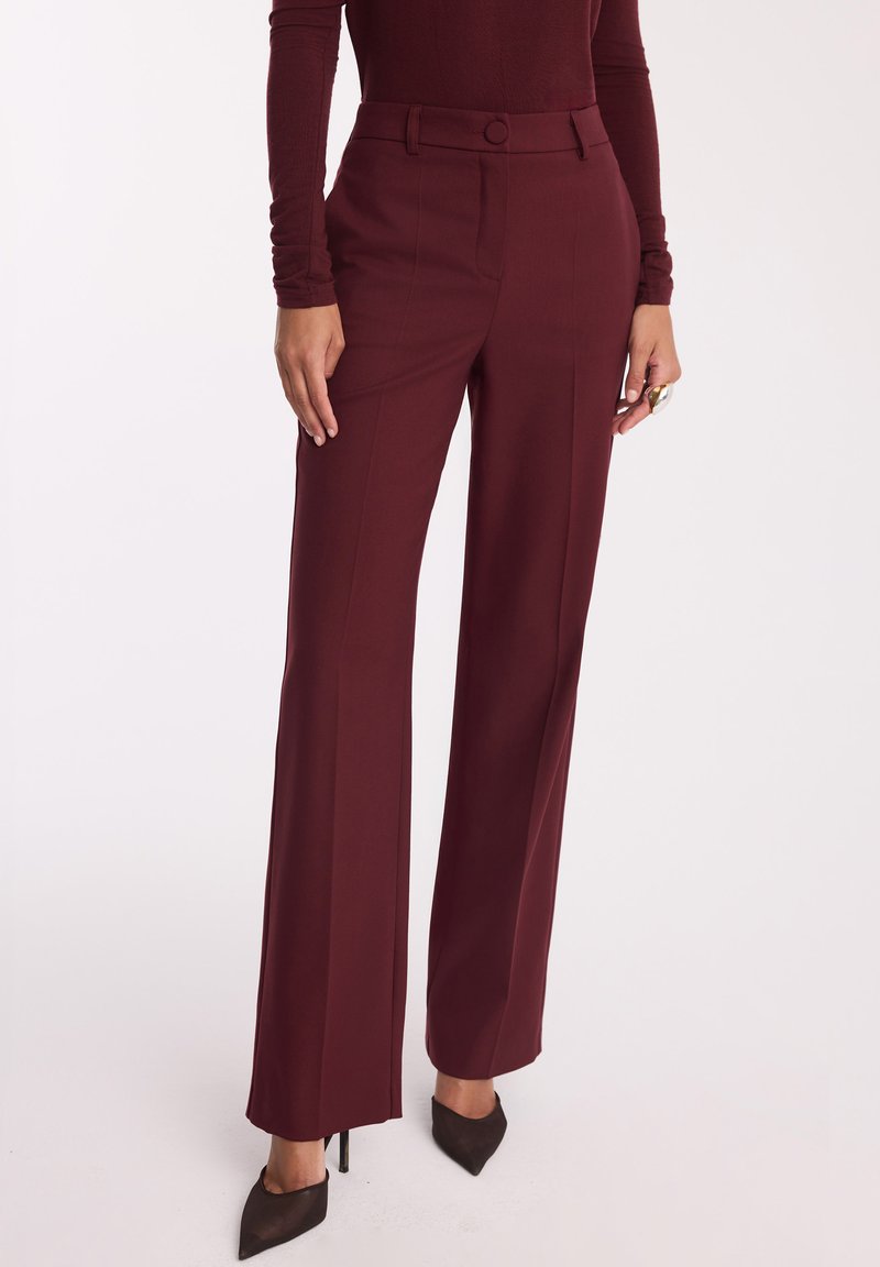 Burgundowe dopasowane spodnie z szerokimi nogawkami, z zapięciem na guzik i szlufkami na pasek. Wykonane z gładkiego materiału, z wyraźnymi fałdami z przodu i bocznymi kieszeniami.