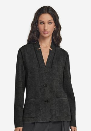 Zwarte geruite blazer met een diepe V-hals, twee voorzakken en knoopsluiting. Textuurstof met een subtiel ruitpatroon.