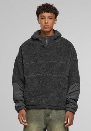 Fleece pullover i mørkegrå, med en halv lynlås i halsen, kontrastfarvede glatte ærmer og en tekstureret krop med et patch-logo detalje.