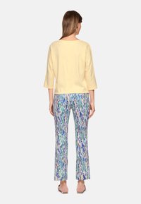 Yellow, three-quarter sleeve top paired with colorful, patterned pants featuring green, blue, and beige abstract designs. Smooth texture.