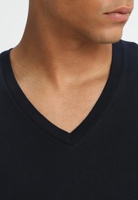 Tricou din bumbac negru cu un design cu gât în formă de V, textură netedă și detalii minime de cusătură, prezentat din zona gâtului în sus.
