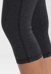 Černé sportovní legíny dlouhé ke kolenům, vyrobené z texturované, elastické látky s hladkým zakončením a jemným melírovaným vzorem.