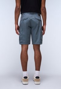 Pantalones cortos cargo de tela gris claro, con dos bolsillos laterales, bolsillos traseros y un corte relajado. Combinados con calcetines blancos y zapatillas.