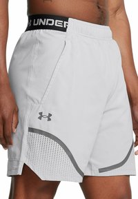 Pantalones cortos deportivos grises con una cinturilla elástica negra etiquetada como "UNDER". Incluyen bolsillos laterales y un patrón de puntos a lo largo del dobladillo.