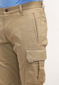 Bermudas de cargo en color beige, con una suave mezcla de algodón, que cuentan con bolsillos laterales, un bolsillo con tapa en el muslo y un bolsillo con cremallera para un almacenamiento seguro.
