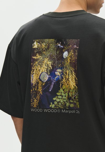 T-shirt noir avec une photo imprimée d'un scooter bleu partiellement couvert de fleurs jaunes et de feuilles vertes au dos.