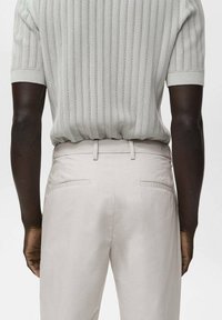 Chemise tricotée gris clair avec une texture côtelée, associée à un pantalon beige ajusté avec des poches arrière et une finition lisse.