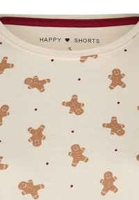 Korte broek van crèmekleurige stof met een patroon van bruine peperkoekfiguurtjes en rode stippen. Rond de hals met een bordeauxrode rand, maat klein.