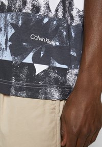 T-shirt z grafiką w ciemnoszarym kolorze z jasnoniebieskim wzorem, z białym logo "Calvin Klein". Wykonany z miękkiej bawełny, luźny krój.