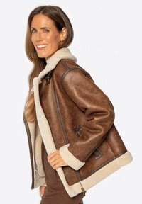 Braune Lederjacke mit Schafslederkragen, durchgehendem Reißverschluss und Seitentaschen. Mit kontrastierenden warmbraunen Akzenten und weicher Textur.