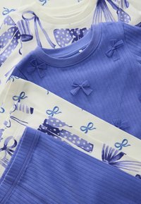 Three tops arranged: one with blue polka dot bows, a deep blue ribbed one with small bows, and a light-colored top featuring blue ribbon patterns.