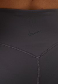 Gros plan sur la taille d'une personne portant un legging noir Nike avec des coutures apparentes et le logo Nike Swoosh sur la ceinture.