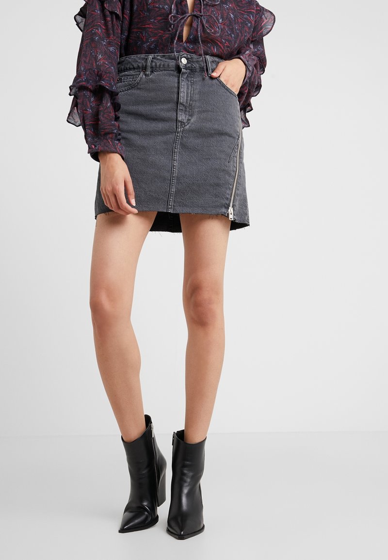 Černá džínová mini sukně s třepeným lemem a bočním zipem. V kombinaci s špičatými černými kotníkovými botami. Volánková blůza s dlouhým rukávem ve tmavých tónech.