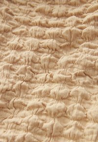 Tissu texturé de couleur beige sable, présentant un motif en relief de formes douces et arrondies créant un effet tactile et ondulé.