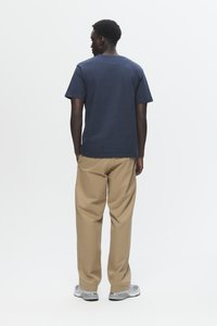 Navy short-sleeve T-shirt with a round neckline, paired with light brown trousers and silver sneakers, viewed from the back.