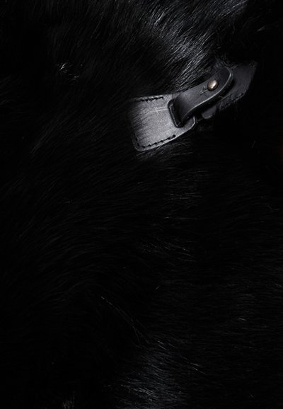 Juodas kailio audinys su minkšta tekstūra, su odiniu dirželiu ir metaliniu užsegimu, pabrėžiančiu turtingą, gilią spalvą.