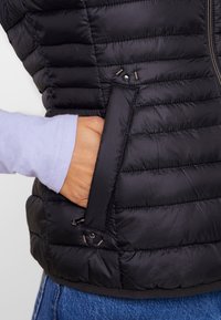 Czarna puchowa kamizelka z poziomym pikowaniem, z boczną kieszenią i zapięciem na zamek. Gładka, błyszcząca tekstura.