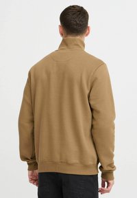 Brown sweatshirt with a high collar, ribbed cuffs and hem, featuring a smooth texture and a minimalist design, shown from the back.