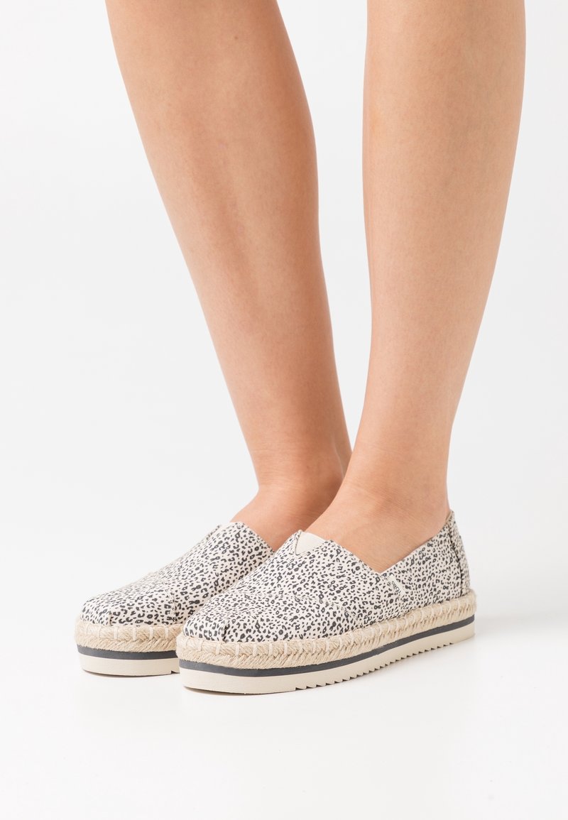 Baskets espadrilles à enfiler avec un motif tacheté noir et blanc, détail en corde de jute autour de la semelle et semelle plate en caoutchouc.