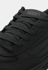 Zwarte sneaker met bovenwerk van stof en leer. Voorzien van dikke zwarte veters, een gevoerde tong en het Vans-logo op de tong. Getextureerde rubberen zool.