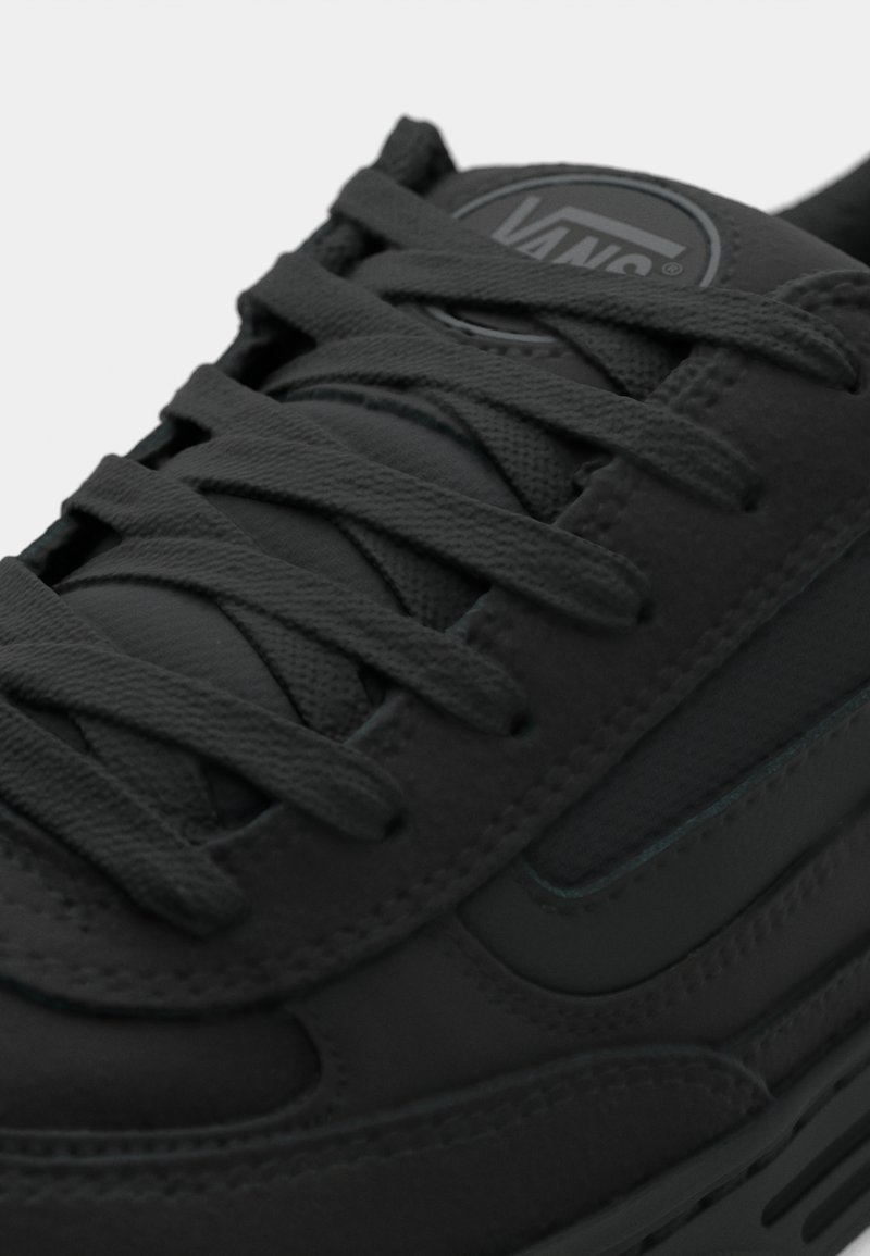 Czarne trampki z cholewką z tkaniny i skóry. Posiadają grube czarne sznurowadła, wyściełany język i logo Vans na języku. Teksturowana gumowa podeszwa.