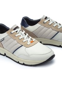 Baskets pour hommes en cuir blanc et textile beige, avec un talon bleu marine, des panneaux texturés et une semelle en caoutchouc noire. Accent orange sur la languette.