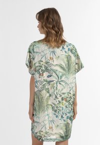Lös passande, kort klänning med ett mönster av gröna tropiska blad på en ljus bakgrund, tillverkad av ett något texturerat, mjukt tyg.