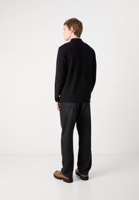 Μαύρο μακρυμάνικο πουκάμισο, άνετη εφαρμογή, φορεμένο με σκούρα γκρι τζιν και καφέ υπόδηση. Απλός σχεδιασμός, χωρίς ορατά μοτίβα ή λεπτομέρειες.