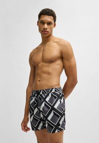 Shorts de bain noirs et gris avec un motif géométrique. Dotés d'une taille élastique et de poches latérales. Matériau léger avec une texture lisse.